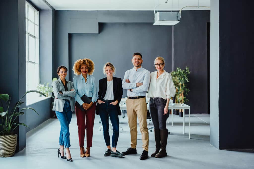 Five professionally dressed team members posing together for a group photo inside a modern office space